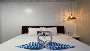 Una habitación de hotel con una cama bien tendida, una lámpara de pared y una decoración de toallas con forma de cisne.