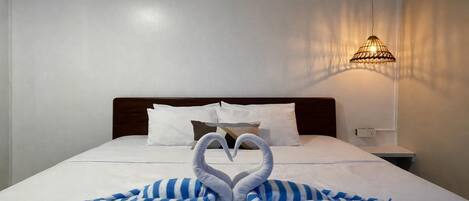 A hotel room with a neatly made bed, a wall-mounted lamp, and a decorative swan towel arrangement.
