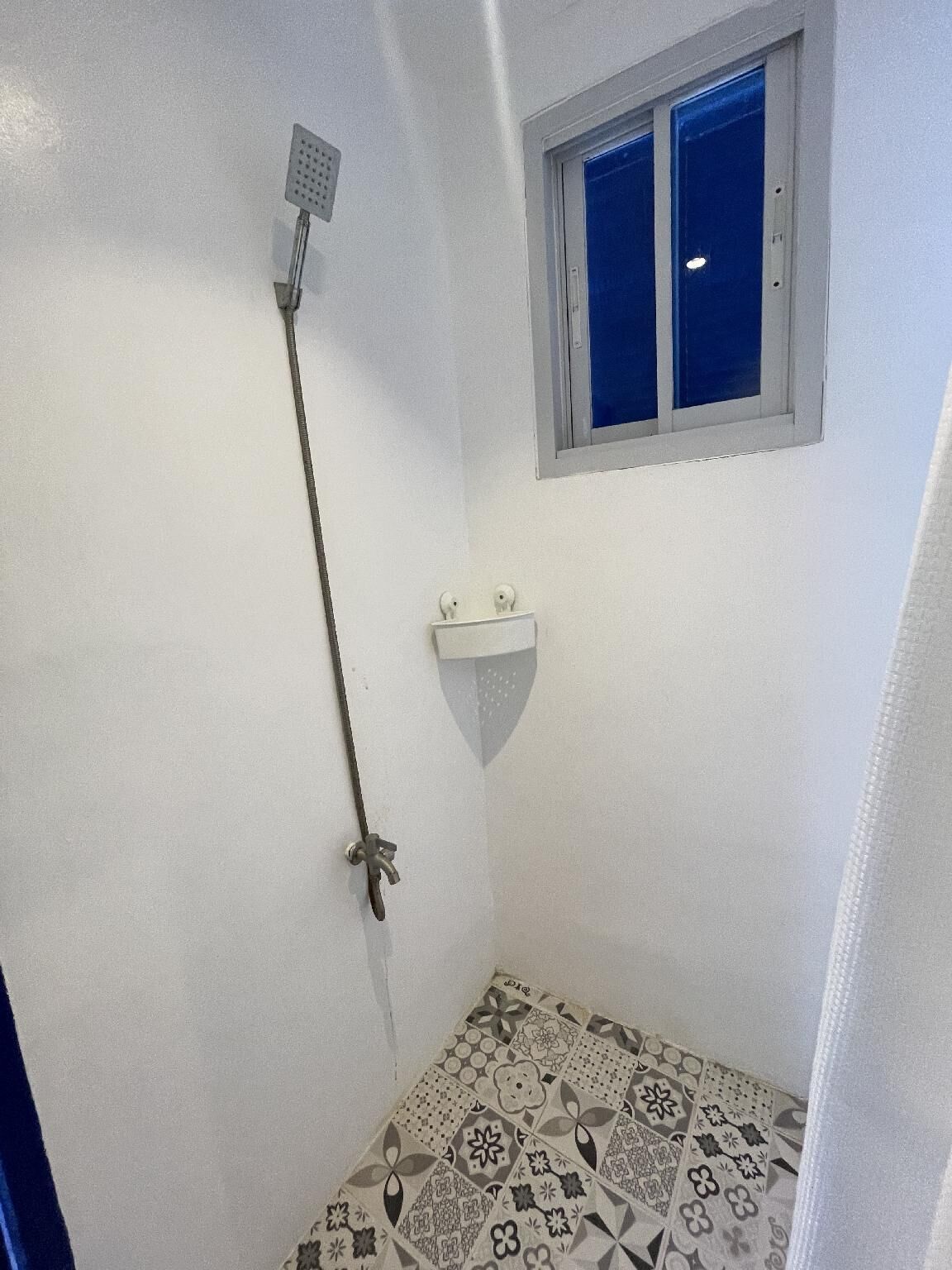 A small bathroom with a shower, a window, and a sink.