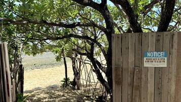 A wooden gate with a notice sign indicating the beach gate is open from 6:00 AM to 6:30 PM for customer safety.