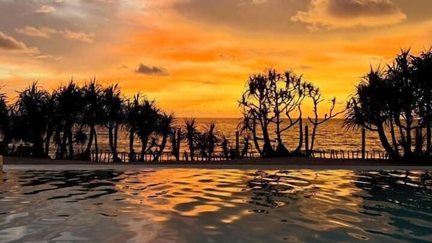 Una vista al atardecer sobre una piscina, con siluetas de árboles y una costa distante.