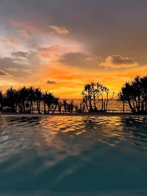 Una vista al atardecer sobre una piscina, con siluetas de árboles y una costa distante.