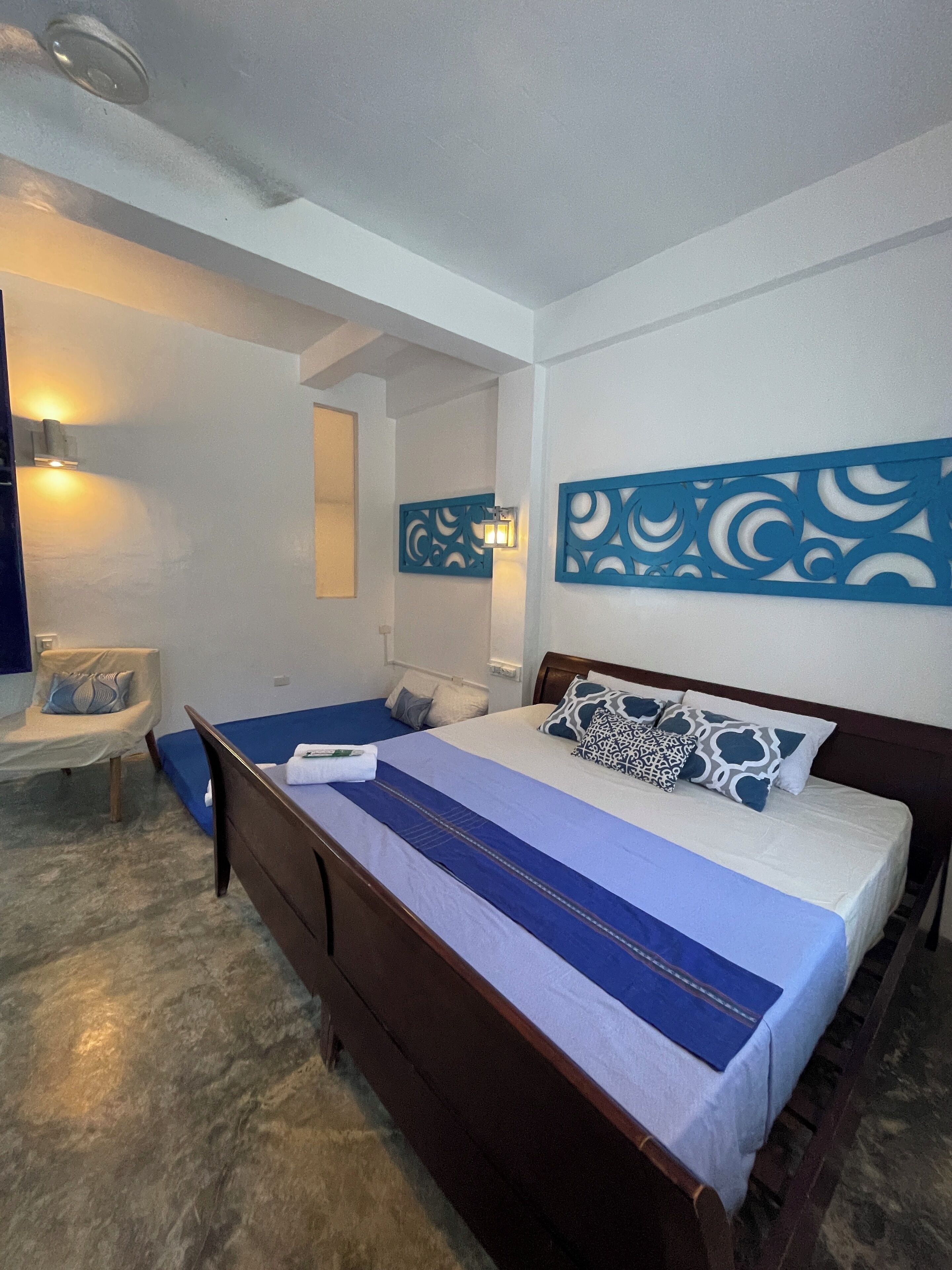 Un dormitorio con una cama grande, una silla y una lámpara fijada a la pared.