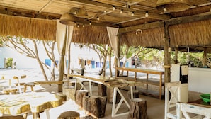 Un restaurante frente al mar con techos de paja, mesas y sillas de madera.