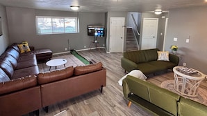 A spacious living room with a brown leather couch, a green sofa, a small round table, and a flat-screen TV on a stand. - 3-BR vacation home with 2 spacious entertaining areas: Sleeps 11, 4 miles to DT (Sioux Falls)