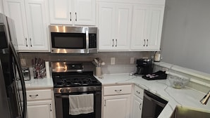 A modern kitchen with white cabinets, stainless steel appliances, and a marble countertop. - 3-BR vacation home with 2 spacious entertaining areas: Sleeps 11, 4 miles to DT (Sioux Falls)