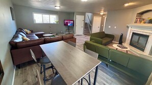 A modern living room with a sectional sofa, a dining table, and a fireplace. - 3-BR vacation home with 2 spacious entertaining areas: Sleeps 11, 4 miles to DT (Sioux Falls)
