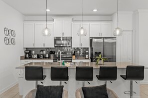 A modern kitchen with white cabinets, stainless steel appliances, and a central island with bar stools. - Modern design near Disney Top resort (Kissimmee)