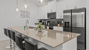 A modern kitchen with white cabinets, stainless steel appliances, and pendant lighting. - Modern design near Disney Top resort (Kissimmee)