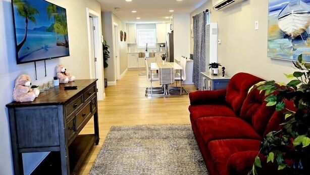 A modern living room with a red sofa, a TV, and a dining area with a kitchen in the background. - 8356 Adam 2bed 2bath back unit by sdstay (Lemon Grove)