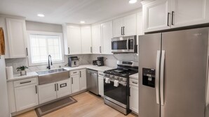 A modern kitchen with white cabinets, stainless steel appliances, a microwave, a stove, and a refrigerator. - 8356 Adam 2bed 2bath back unit by sdstay (Lemon Grove)