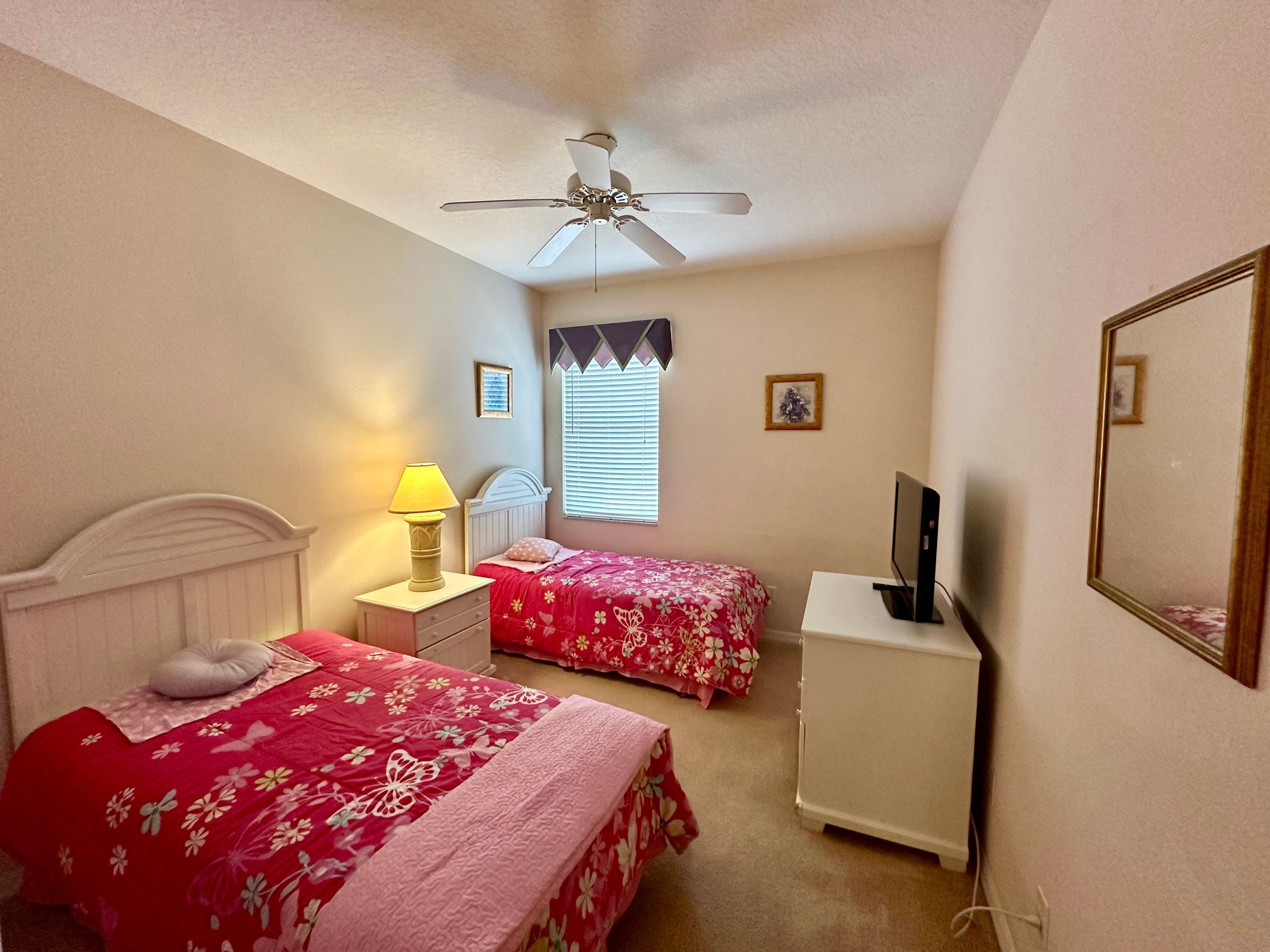 Une chambre avec deux lits, un ventilateur de plafond, un bureau avec un ordinateur et une télévision.