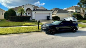 A residential street with houses, a driveway, and a black car parked in front.