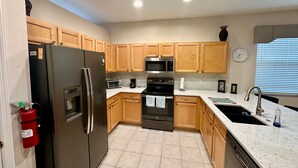 A kitchen with wooden cabinets, a stainless steel refrigerator, a microwave, an oven, and a sink.