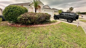 A residential area with a house, a driveway, and a black SUV parked in front.