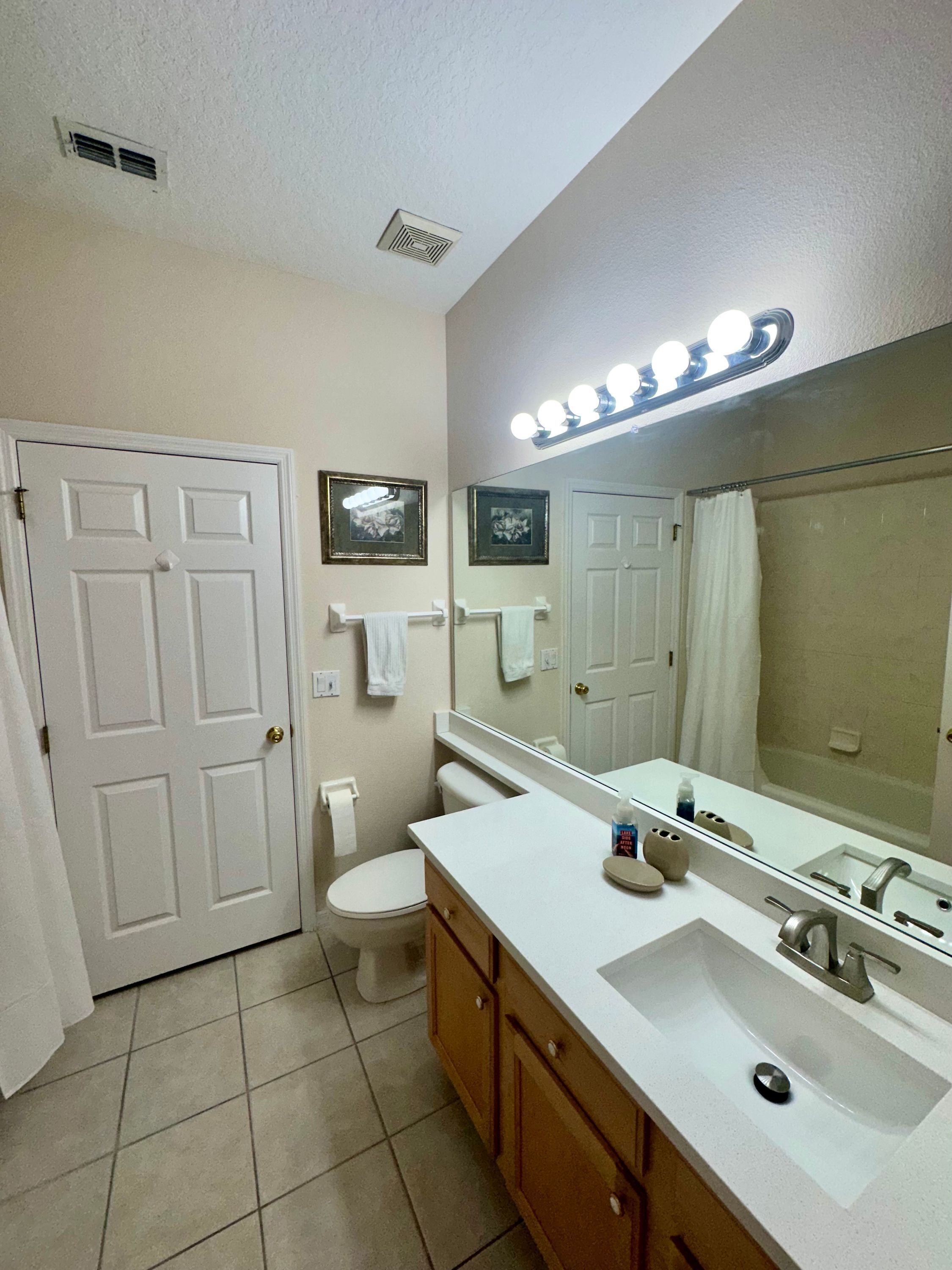 Une salle de bain avec des toilettes blanches, un lavabo avec un miroir et un espace douche.