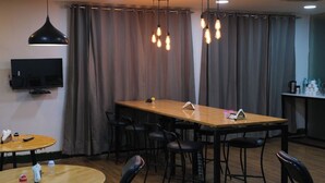 A modern dining area with a wooden table and black chairs, a flat-screen TV mounted on the wall, and a kitchen area with a counter and various items. - Lime Tree Premier Near Medanta Medicity (Gurugram)