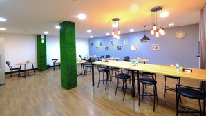 A conference room with multiple tables and chairs, a green artificial column, and ceiling lights. - Lime Tree Premier Near Medanta Medicity (Gurugram)