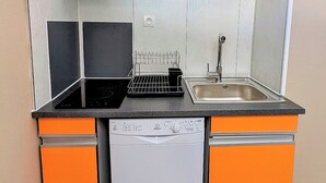 A compact kitchen with orange cabinetry, a black induction cooktop, a white dishwasher, and a sink. - Apartment close to port, beaches, golf course and ile des Loisirs with air conditioning (Agde)