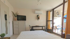 A bedroom with a bed, a desk, a chair, a TV, and an air conditioning unit. - Apartment close to port, beaches, golf course and ile des Loisirs with air conditioning (Agde)