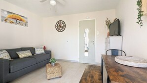 A living room with a gray sofa, a wooden coffee table, a small woven stool, a clock, and a door with a mirror. - Apartment close to port, beaches, golf course and ile des Loisirs with air conditioning (Agde)