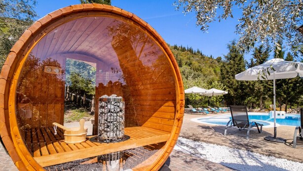 A wooden barrel-shaped room with a stone fireplace, wooden bench, and a view of a pool and lounge chairs. - Peaceful Villa at Apanema Mindfulness Lefkada (Sfakiotes)