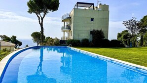 A swimming pool with a clear blue water surface, surrounded by a well-maintained lawn and a building with a balcony.