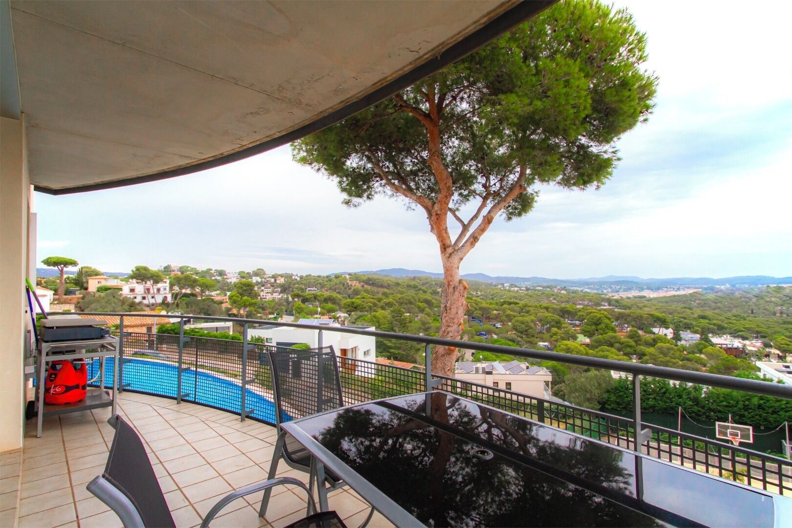 A balcony with a pool, outdoor furniture, and a view of a tree and landscape.