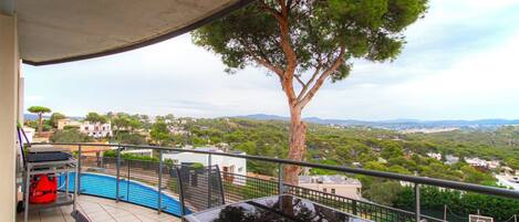 A balcony with a pool, outdoor furniture, and a view of a tree and landscape.