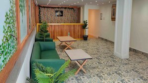 Um saguão de hotel com balcão de recepção, sofás verdes, uma mesinha e um tapete estampado.