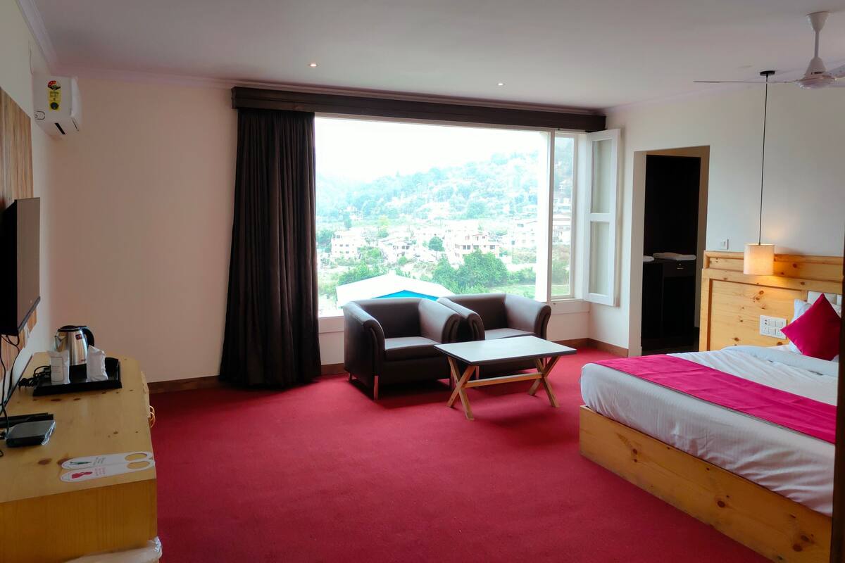 Ein Hotelzimmer mit Bett, Schreibtisch, Stuhl, Fenster mit Blick auf Gebäude und Deckenventilator.