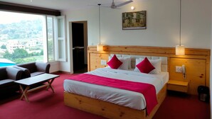 Quarto de hotel com cama, escrivaninha, cadeira, ventoinha no teto e janela com vista para edifícios e áreas verdes.