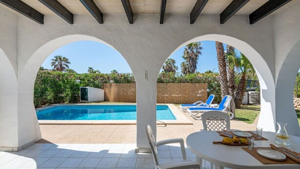 An outdoor pool area with a covered patio, white walls, and a view of the pool. - Villa Flor, relax in Menorca (Cap d`Artrutx)