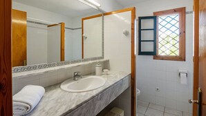 A bathroom with a marble sink, a large mirror, and a window with a lattice design. - Villa Flor, relax in Menorca (Cap d`Artrutx)