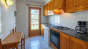 A kitchen with wooden cabinets, a gas stove, a coffee maker, and a dining table. - Villa Flor, relax in Menorca (Cap d`Artrutx)