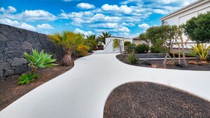A modern pathway leading to a building with a stone wall on one side and a variety of plants. - Villa Endless Summer - Pool and BBQ By LVH (Playa Blanca)