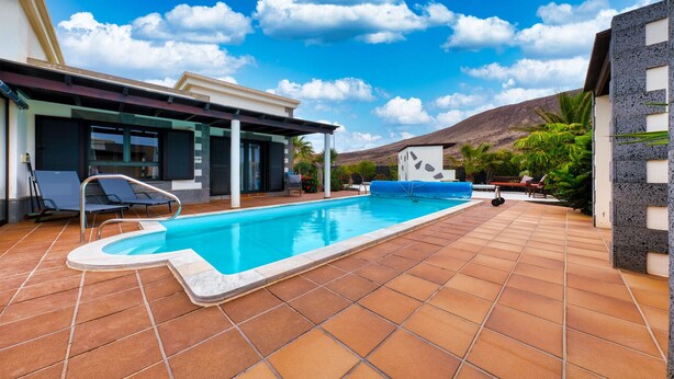 A swimming pool with a tiled deck, a covered area with chairs, and a mountain in the background. - Villa Endless Summer - Pool and BBQ By LVH (Playa Blanca)