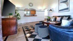 A modern living room with a flat-screen TV, a sofa, ottomans, a kitchen area, and a clock on the wall. - Villa Endless Summer - Pool and BBQ By LVH (Playa Blanca)