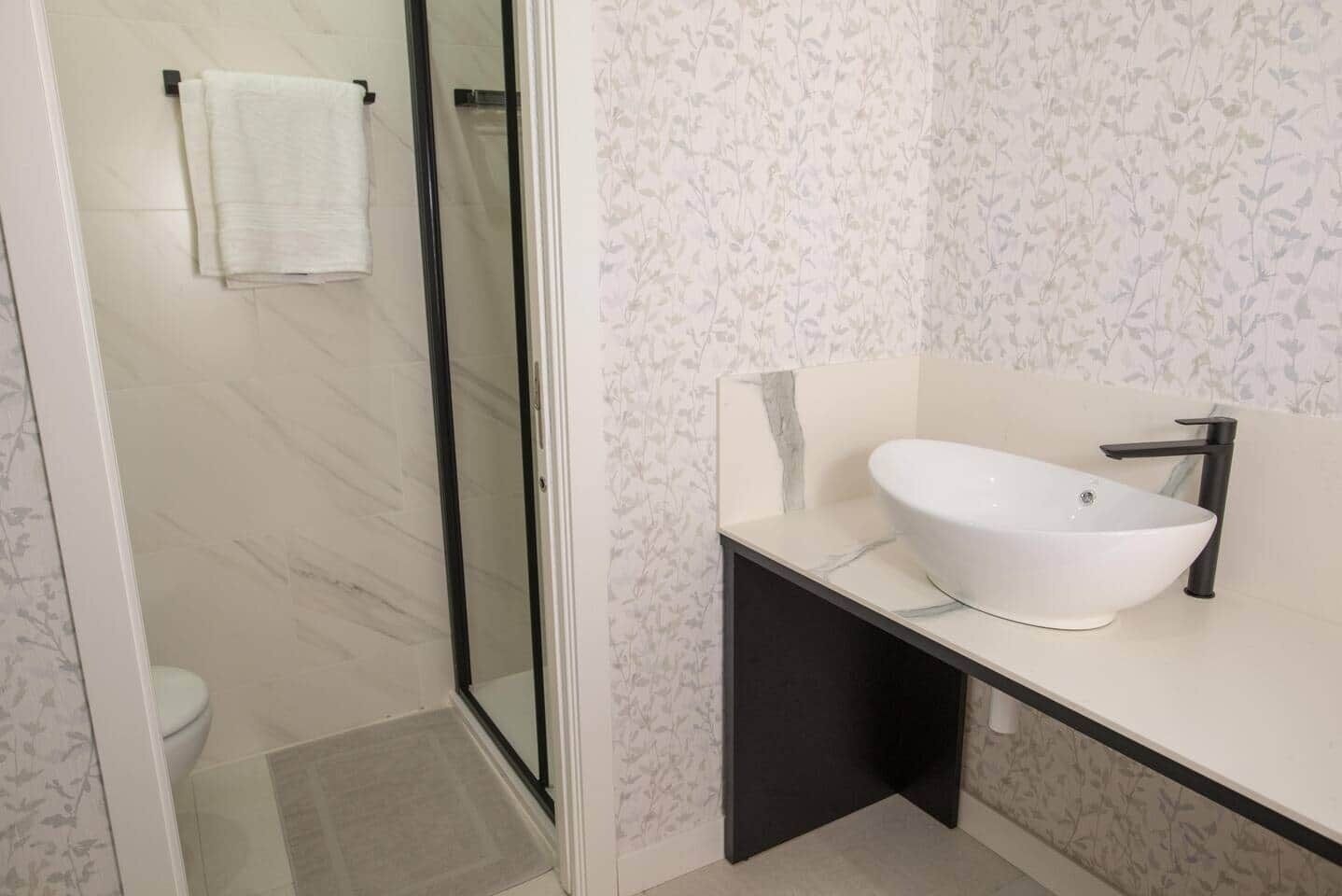 Et moderne badeværelse med en brusekabine i glas, en hvid vask med sort armatur og et toilet.