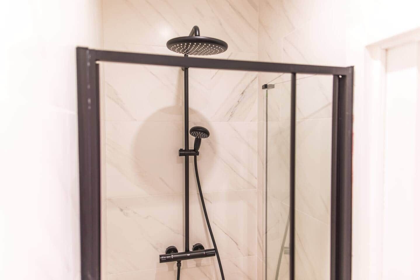 A modern shower enclosure with a rain showerhead and handheld showerhead, set against a marble wall.