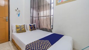 A neatly made bed with patterned pillows, a blue and yellow blanket, and a window with sheer curtains. - OYO Life 94040 Agung Home Stay (Surabaya)