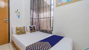 A neatly made bed with patterned pillows, a blue and yellow blanket, and a window with sheer curtains.