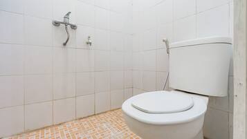 Un baño con inodoro blanco, ducha con grifo empotrado en la pared y suelo de baldosas.