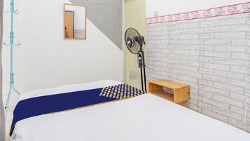 Un dormitorio con cama, ventilador, perchero y un pequeño estante de madera.