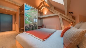 A bedroom with a large bed, a wooden ceiling, a view of a landscape through a window, and a door. - Domaine Carrel & Senger (Jongieux)