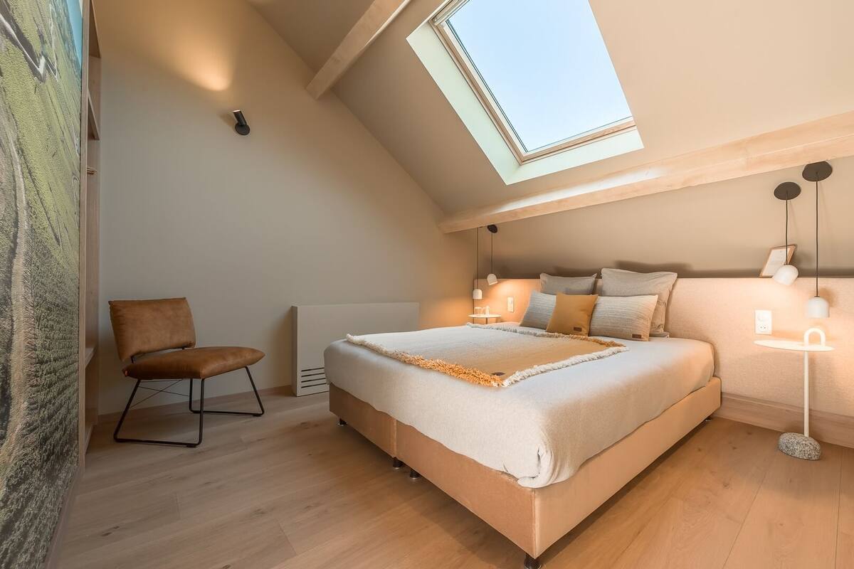 Une chambre à coucher avec un puits de lumière, un lit, une chaise et des lampes de chevet.