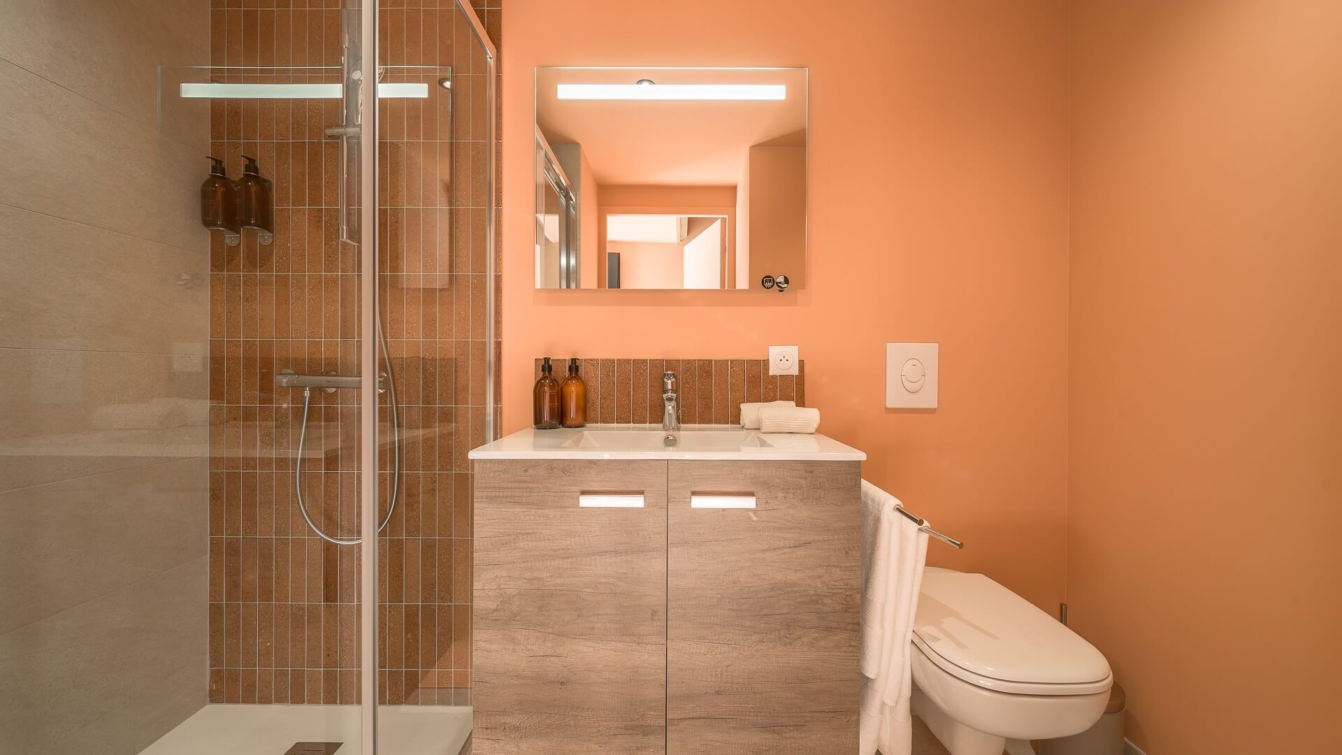 A bathroom with a glass-enclosed shower, a sink with a mirror above it, and a toilet.