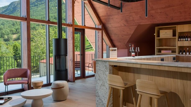 Zona de bar moderna con mostrador de madera, asientos y vistas a follaje exuberante.