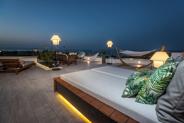 A rooftop terrace with a bed, lounge chairs, and ambient lighting.