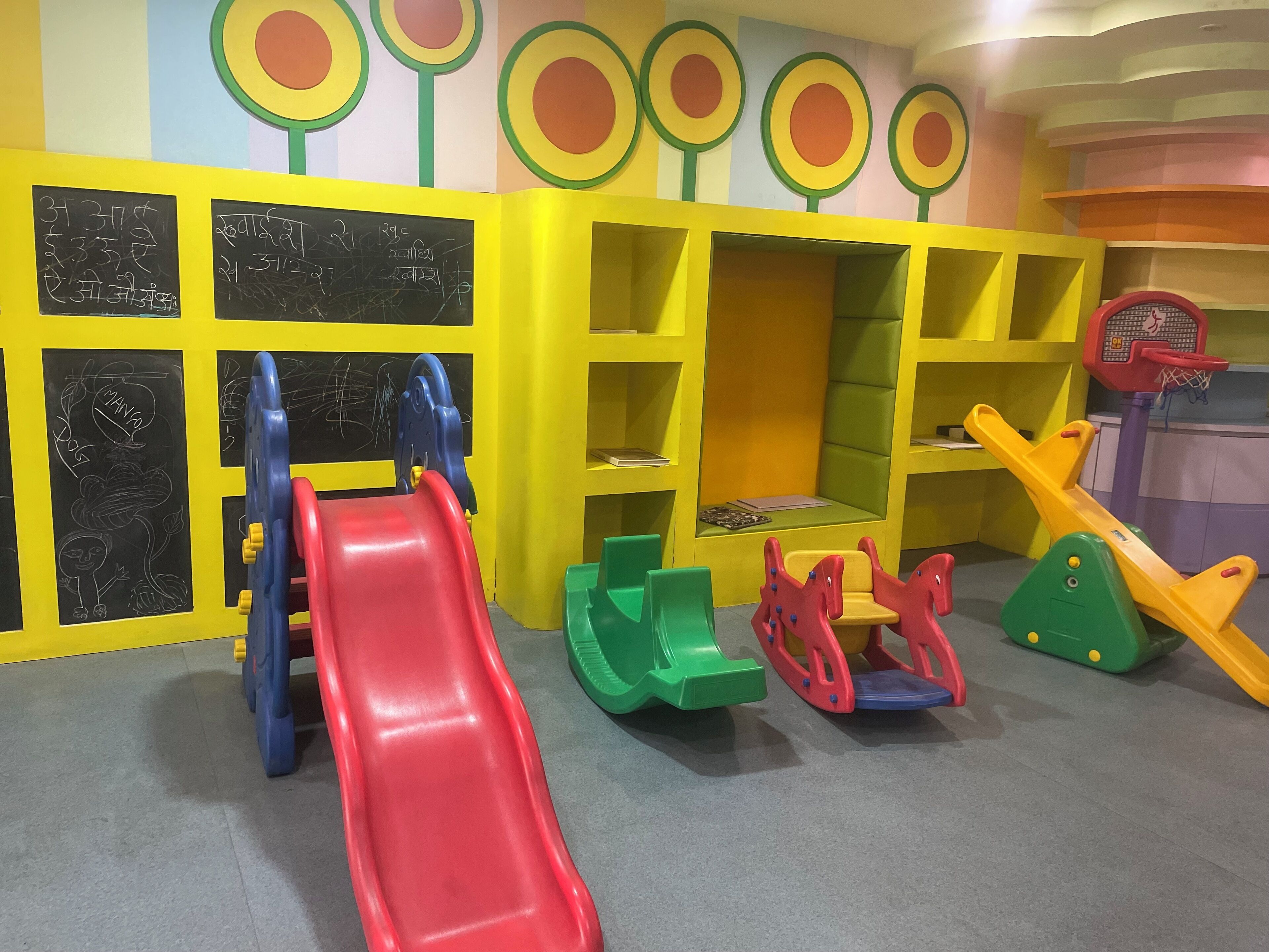 A children's play area with a red slide, climbing structures, and chalkboard walls.